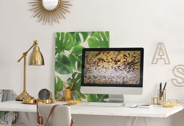 Modern workplace with computer and golden decor on desk near wall. Stylish interior design