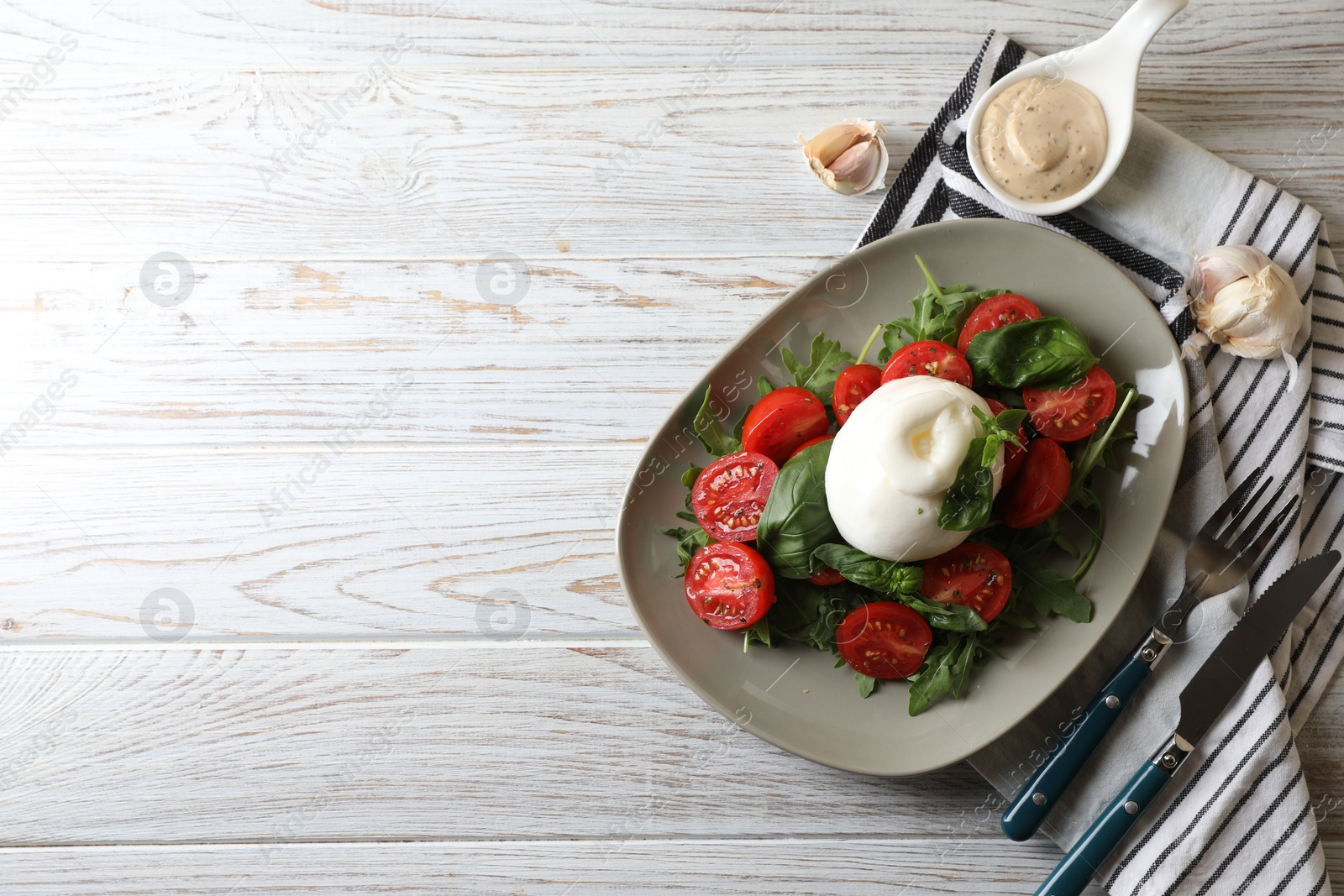 Photo of Delicious burrata cheese served with tomatoes and basil on white wooden table, flat lay. Space for text