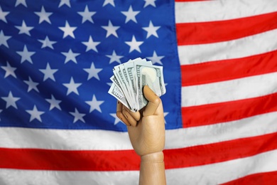 Wooden mannequin hand with fan of banknotes against USA national flag