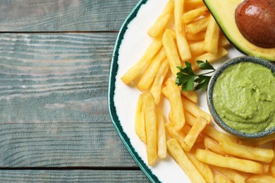Photo of Plate with french fries, guacamole dip, parsley and avocado served on grey wooden table, top view. Space for text