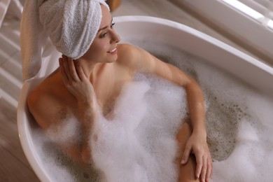 Photo of Beautiful woman taking bath in tub with foam indoors, top view