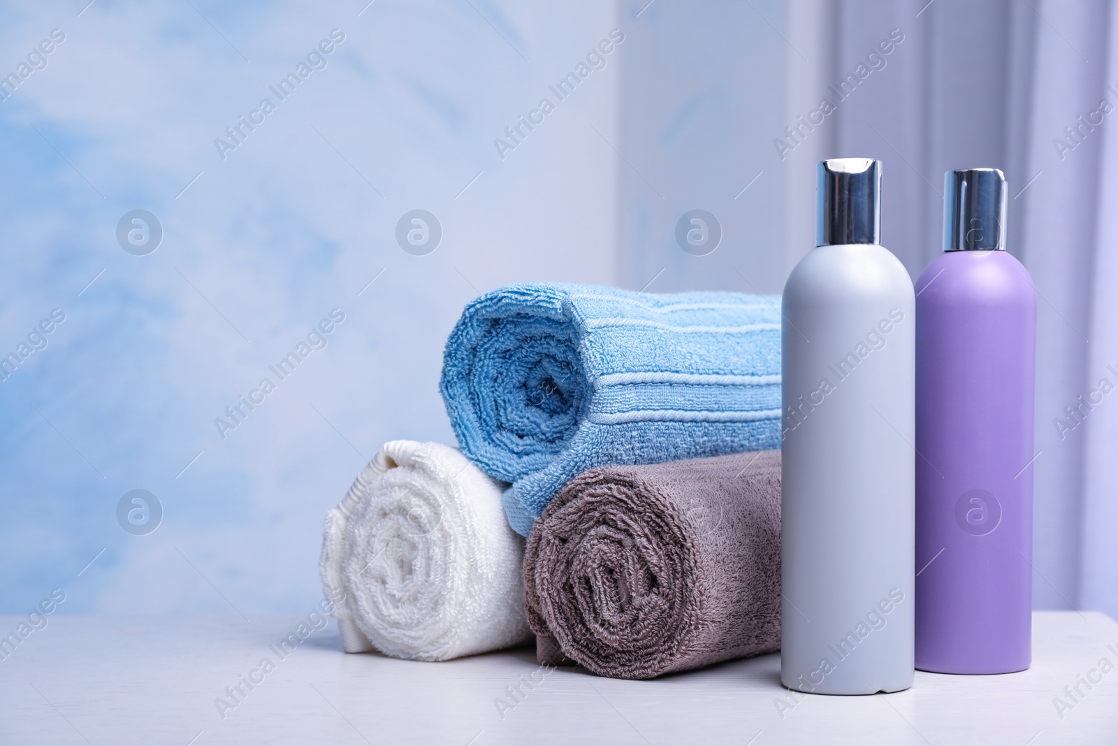 Photo of Bottles of shampoo and rolled bath towels on table, space for text