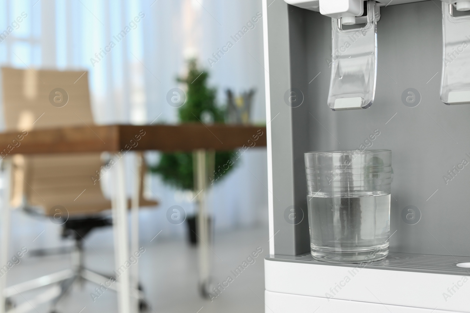 Photo of Modern water cooler with glass in office, closeup. Space for text