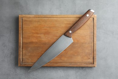 Photo of Knife and wooden board on grey textured table, top view