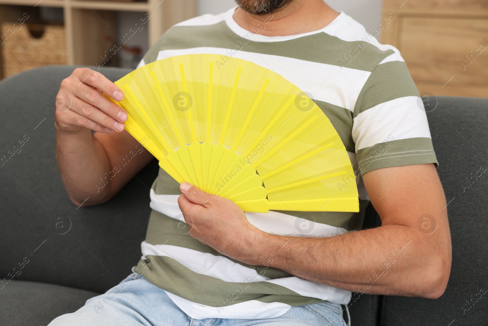 Photo of Man with yellow hand fan on sofa at home, closeup