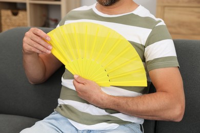 Man with yellow hand fan on sofa at home, closeup