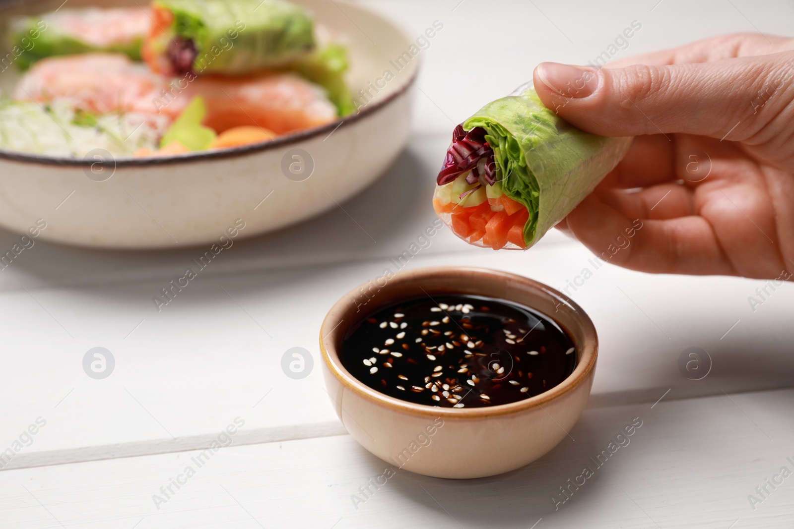 Photo of Woman eating delicious spring roll wrapped in rice paper with sauce at white wooden table, closeup. Space for text