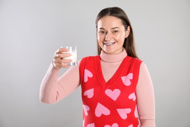 Photo of Happy woman with milk mustache holding glass of drink on light grey background