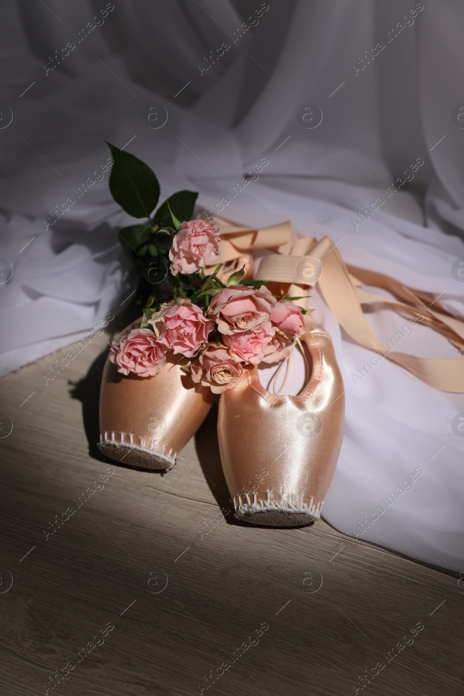 Photo of Ballet shoes. Elegant pointes and bouquet of roses on wooden floor