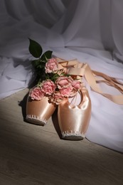 Photo of Ballet shoes. Elegant pointes and bouquet of roses on wooden floor
