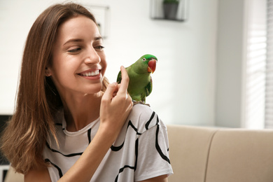 Young woman with cute Alexandrine parakeet indoors