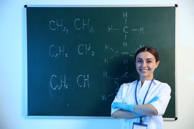 Photo of Female scientist standing near chalkboard with chemical formulas indoors