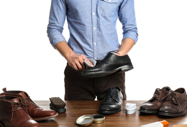 Man cleaning leather shoe at wooden table against white background, closeup