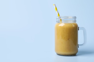 Photo of Mason jar with delicious fruit smoothie on light blue background. Space for text