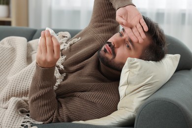 Sick man with tissue lying on sofa at home. Cold symptoms