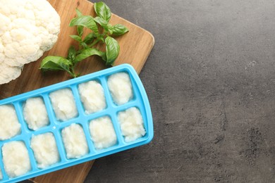 Cauliflower puree in ice cube tray ready for freezing and ingredients on grey table, flat lay. Space for text