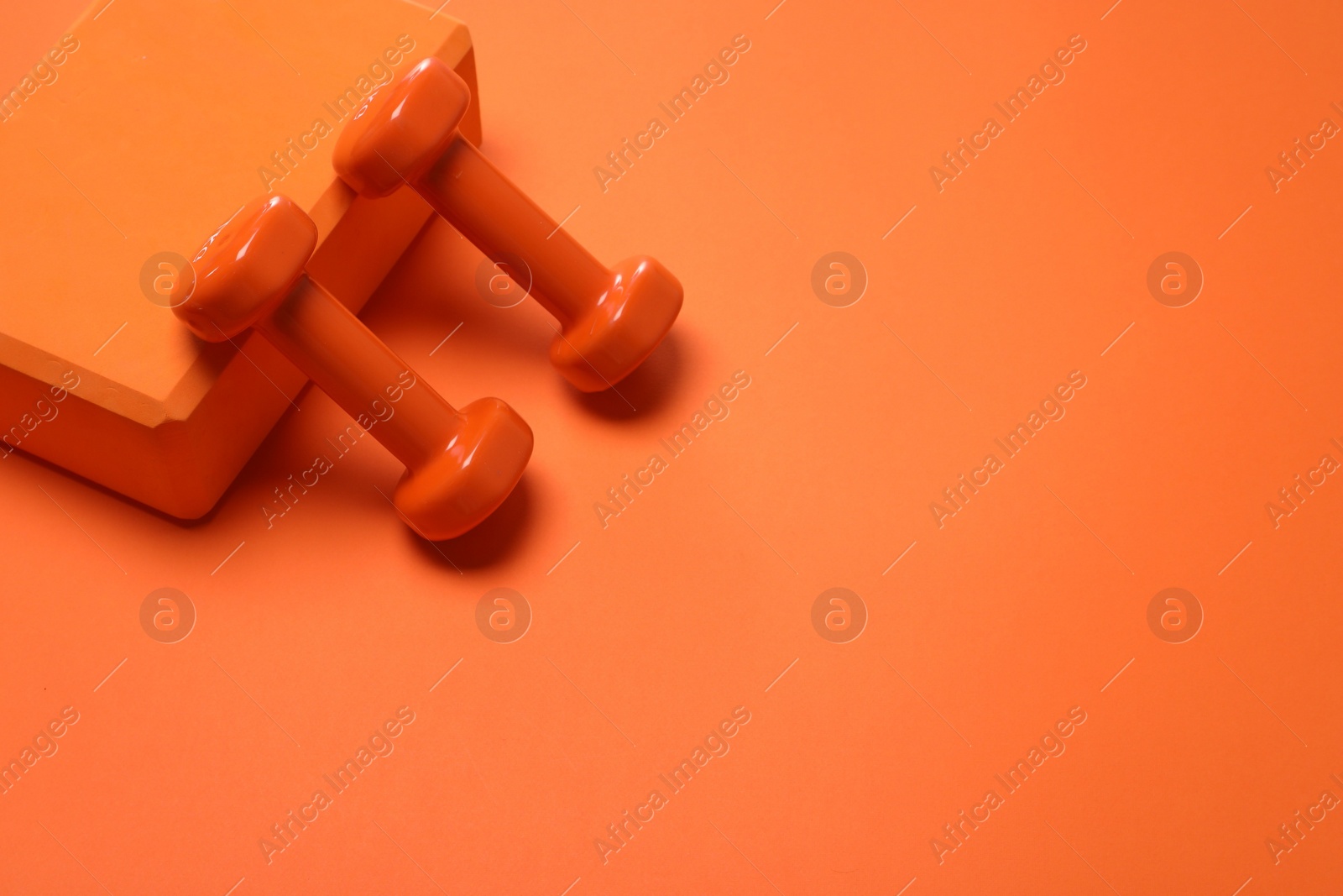 Photo of Dumbbells and yoga block on orange background. Space for text