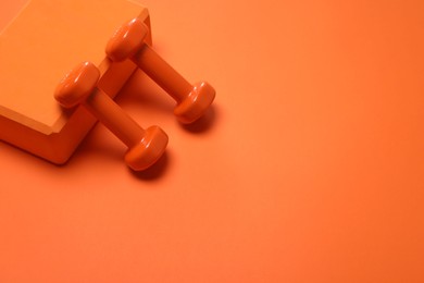 Photo of Dumbbells and yoga block on orange background. Space for text