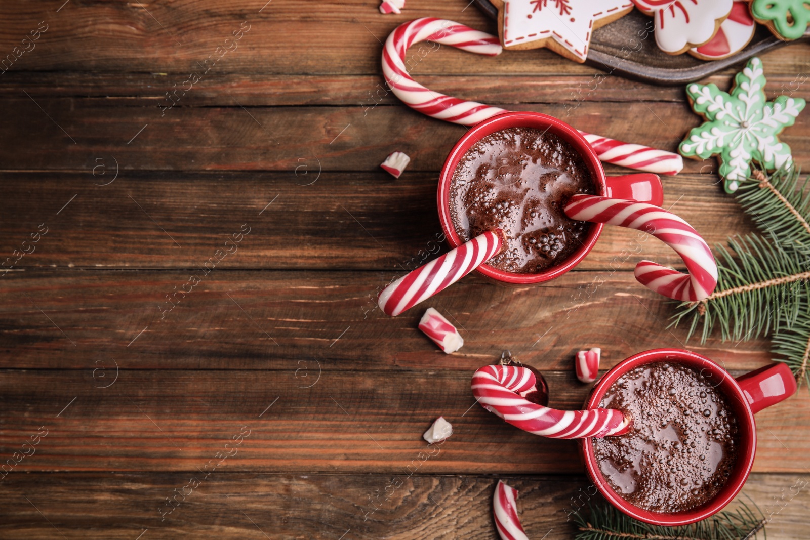 Photo of Flat lay composition with cups of hot chocolate and Christmas candy canes on wooden table. Space for text