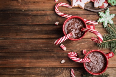 Photo of Flat lay composition with cups of hot chocolate and Christmas candy canes on wooden table. Space for text