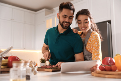 Photo of Lovely young couple with tablet cooking together in kitchen