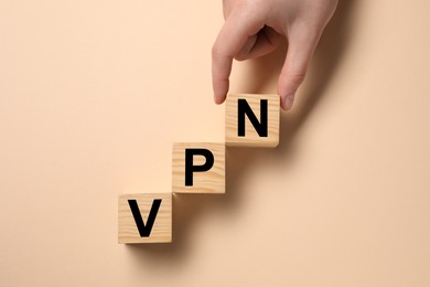 Photo of Woman making acronym VPN with wooden cubes on beige background, top view