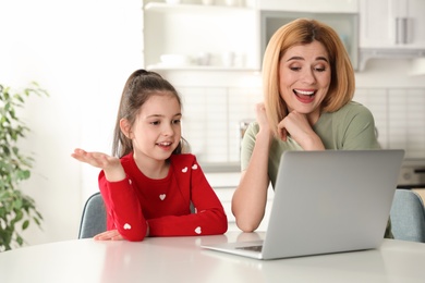 Photo of Mother and her daughter using video chat on laptop at table in kitchen