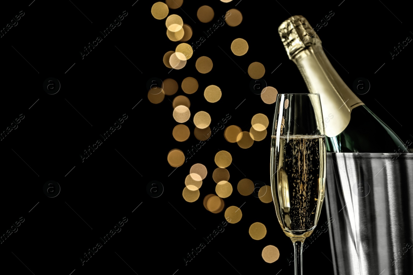 Photo of Glass of champagne near bucket with bottle against blurred lights, space for text