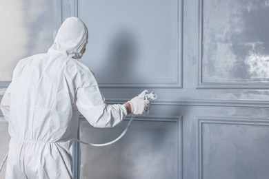 Decorator dyeing wall in grey color with spray paint, back view