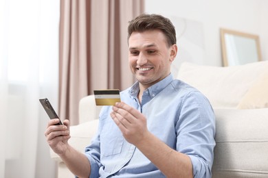 Photo of Happy man with credit card using smartphone for shopping online at home