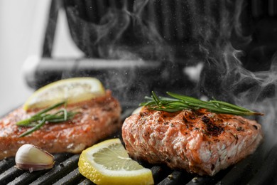 Photo of Tasty salmon cooking with rosemary and lemon slice on electric grill, closeup