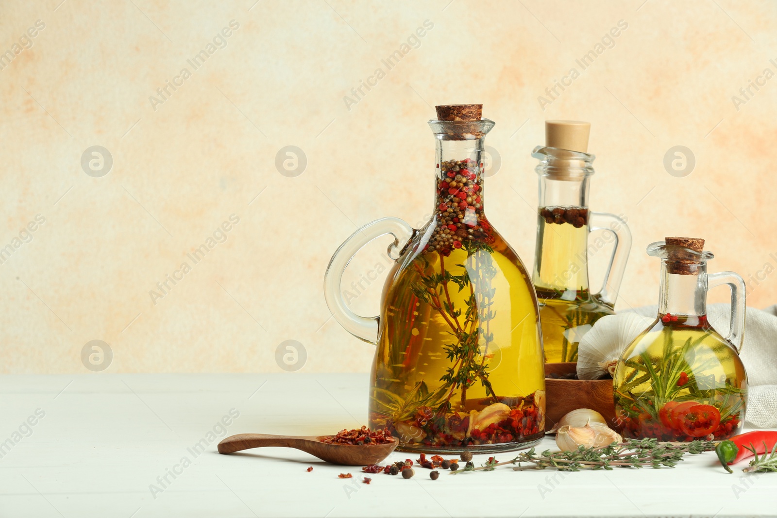 Photo of Cooking oil with different spices and herbs in jugs on white wooden table. Space for text