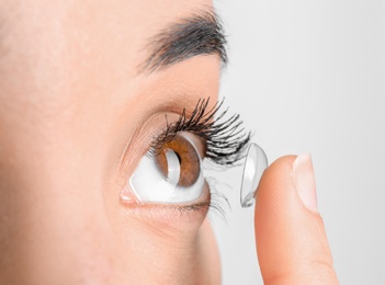 Photo of Young woman putting contact lens in her eye, closeup