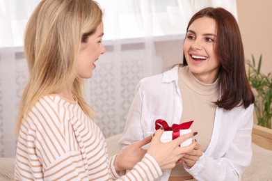 Smiling young woman presenting gift to her friend at home