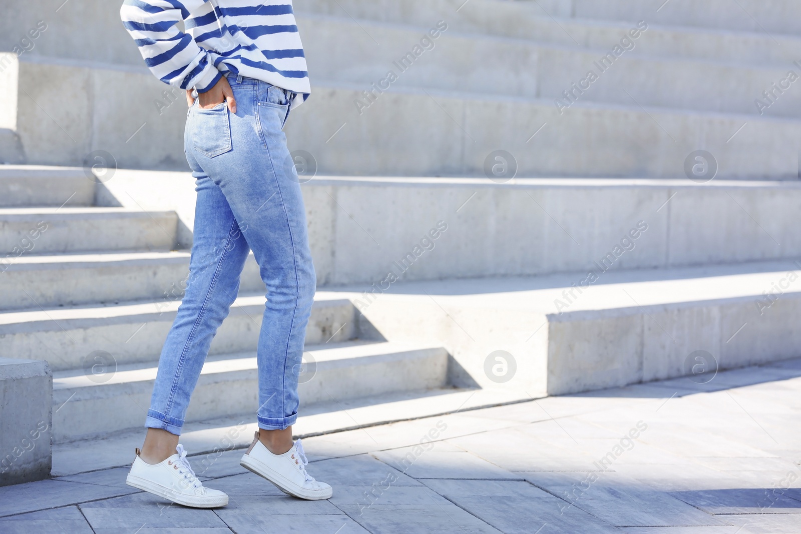 Photo of Young hipster woman in stylish jeans standing near stairs outdoors