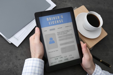 Man holding tablet with driver's license application form at grey table, closeup