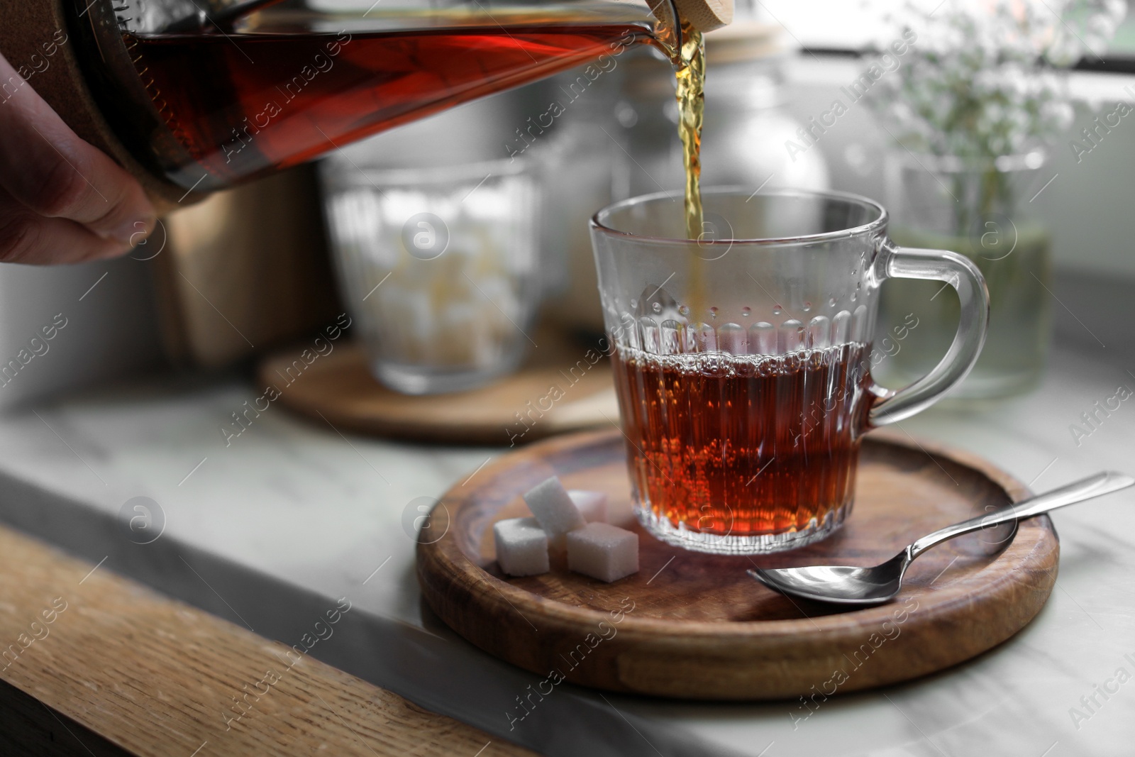 Photo of Woman pouring delicious tea into glass cup at table, closeup