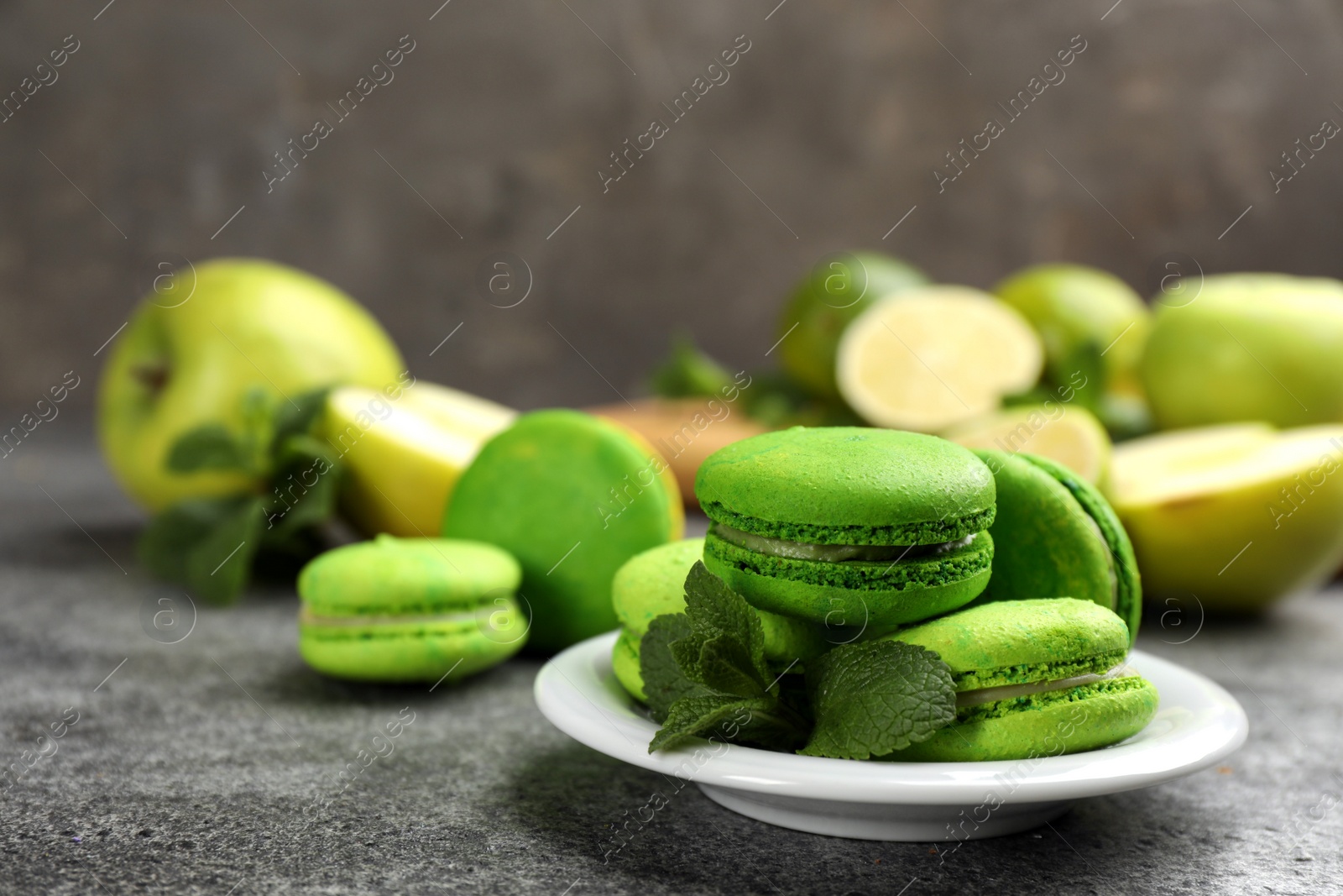 Photo of Delicious macarons, mint and fruits on grey table