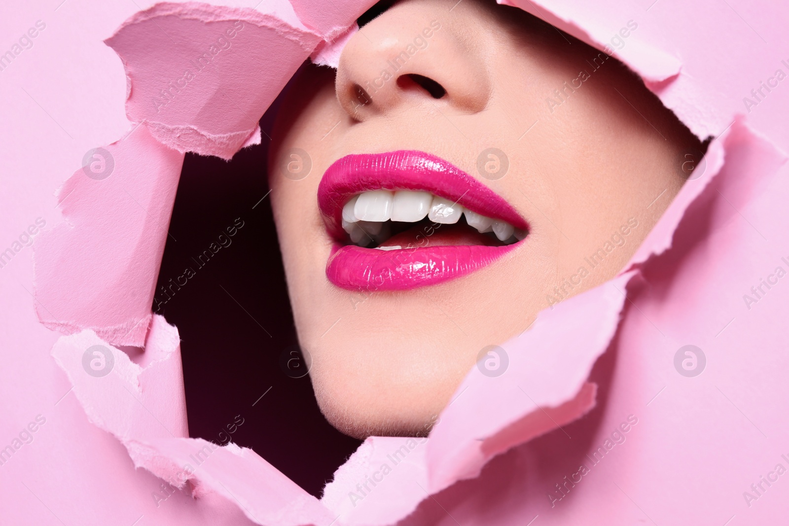 Photo of View of beautiful young woman with perfect lips makeup through hole in color paper