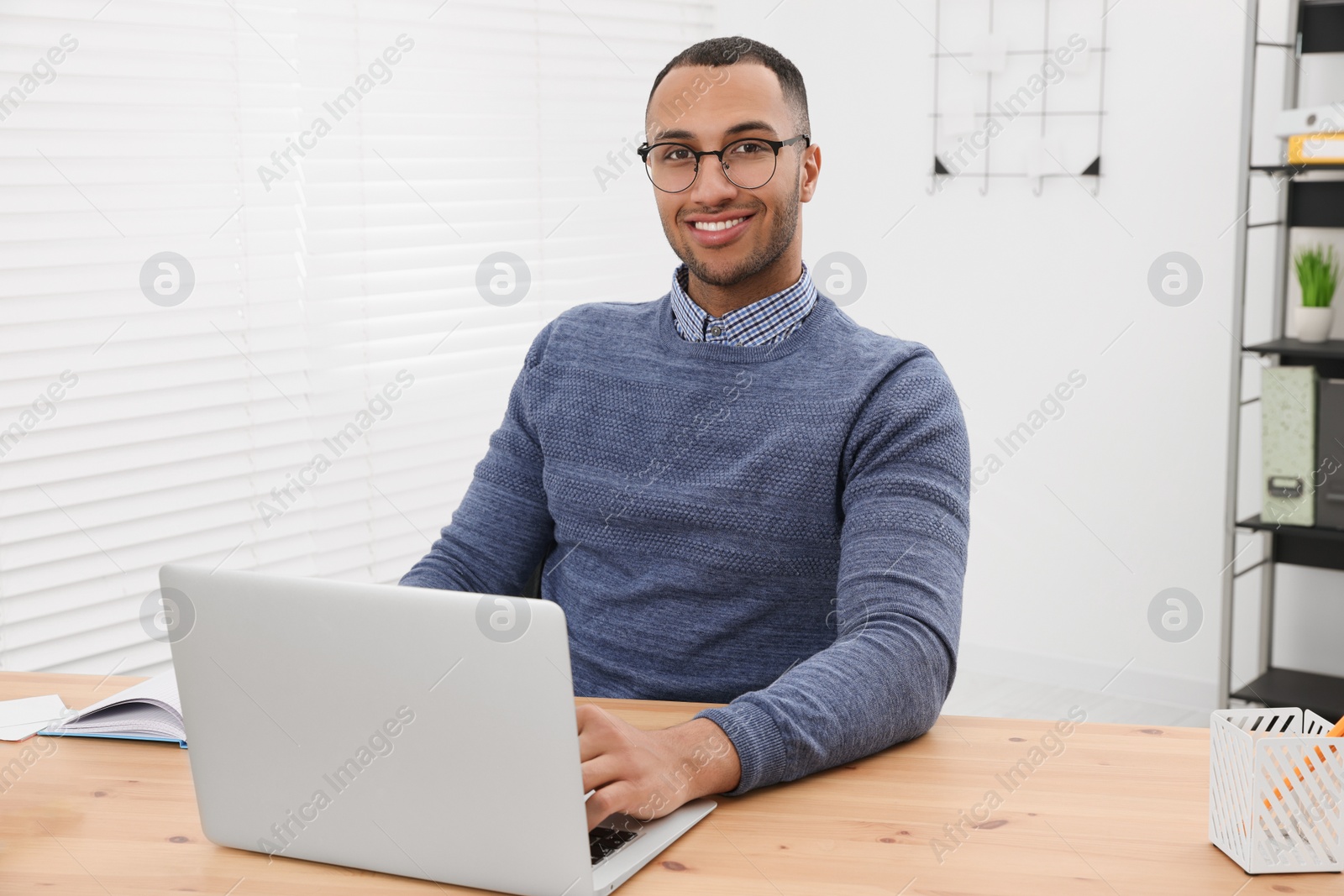 Photo of Happy young intern working with laptop at table in modern office