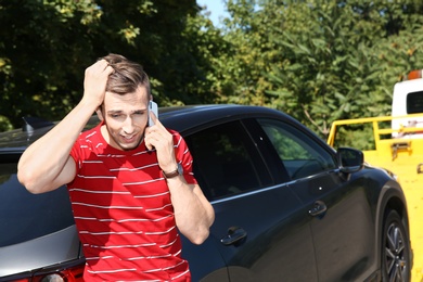 Photo of Man talking on phone near broken car and tow truck outdoors
