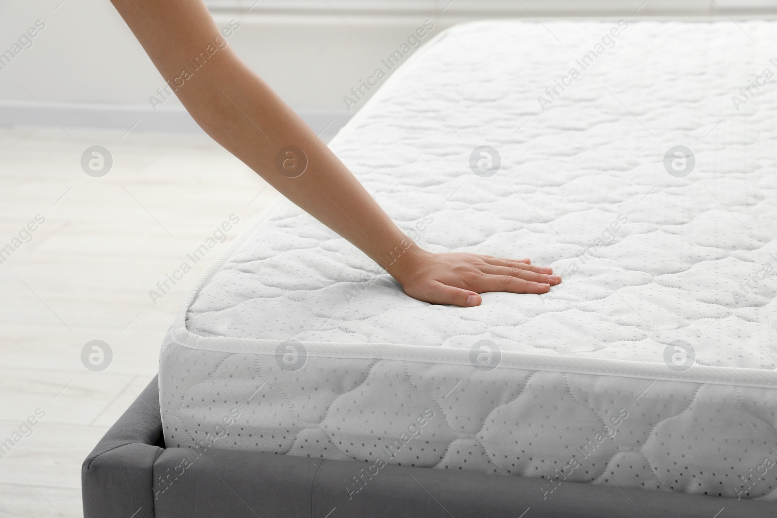 Photo of Woman touching soft light green mattress indoors, closeup