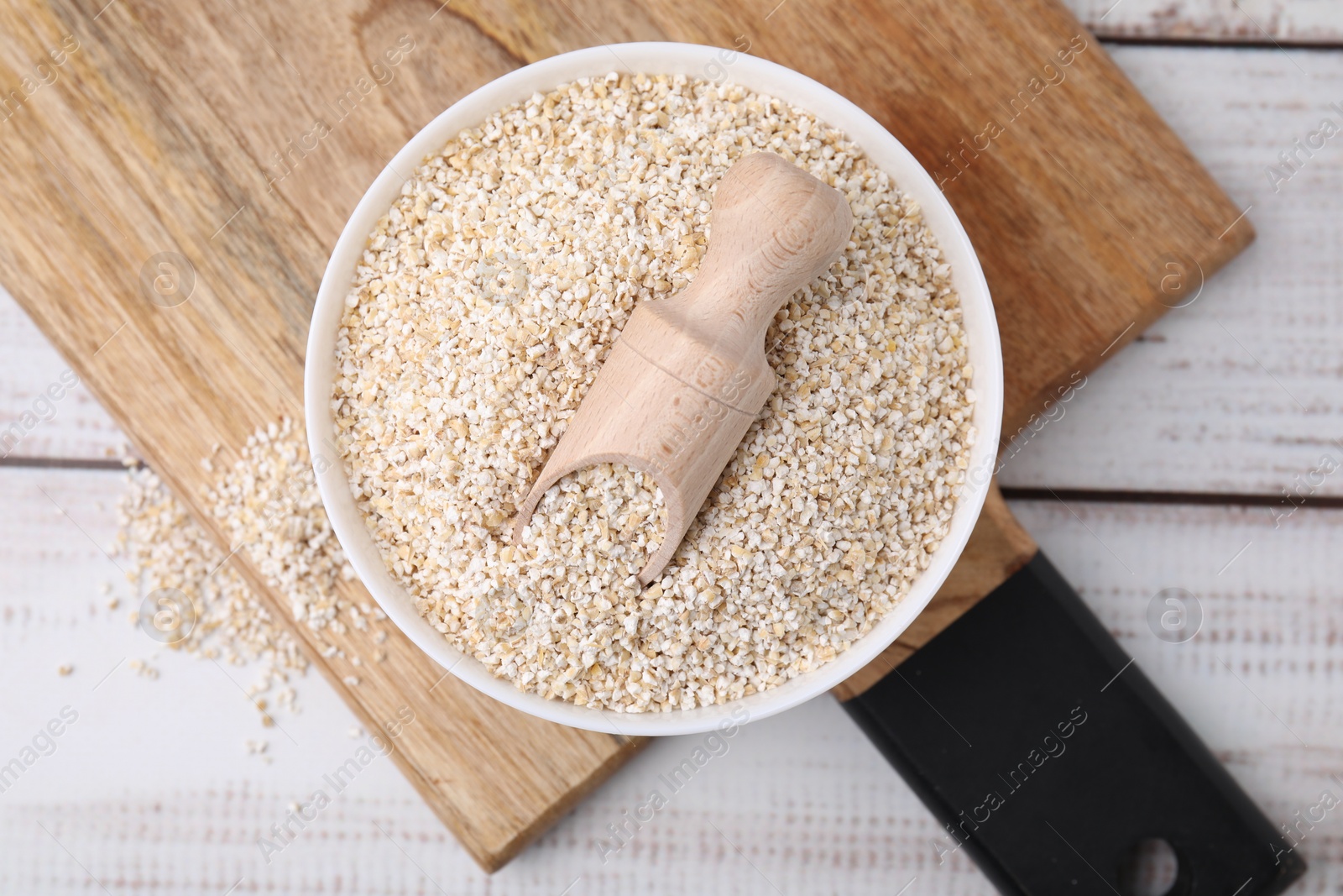 Photo of Raw barley groats and scoop in bowl on light wooden table, top view