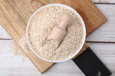 Photo of Raw barley groats and scoop in bowl on light wooden table, top view