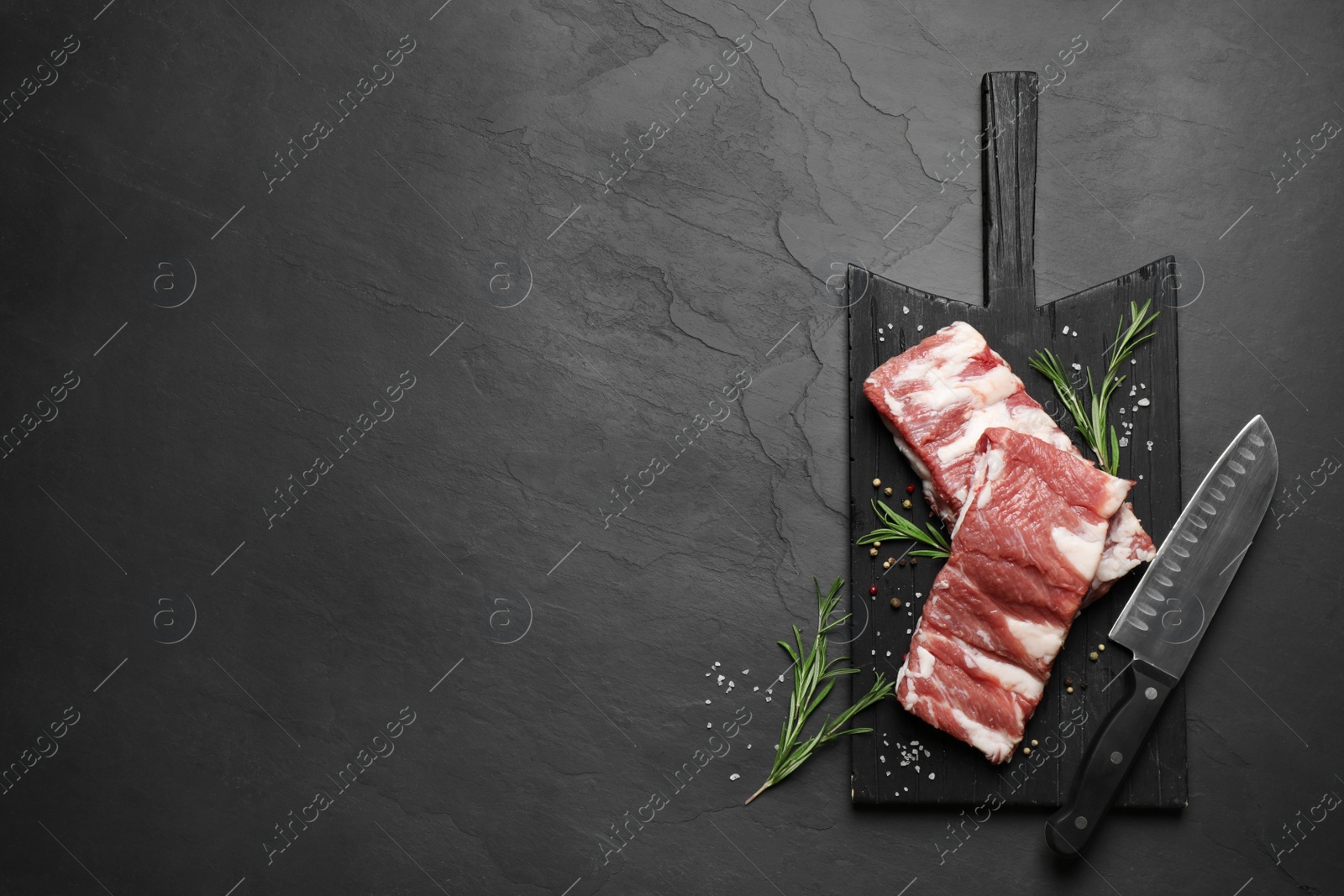 Photo of Raw ribs with rosemary and spices on black table, top view. Space for text