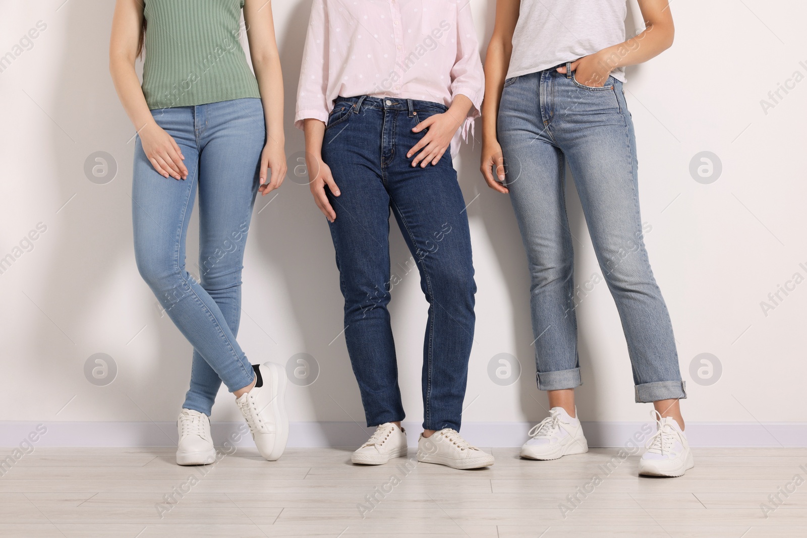 Photo of Women in stylish jeans near white wall, closeup