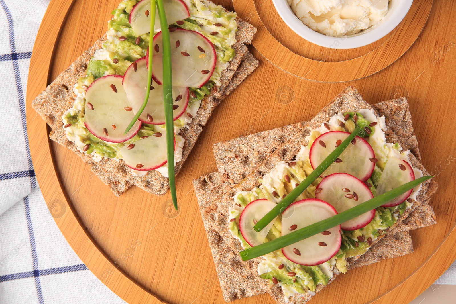 Photo of Fresh crunchy crispbreads with cream cheese, radish and green onion on wooden board, top view