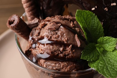 Delicious chocolate ice cream with wafer sticks and mint in glass dessert bowl on table, closeup