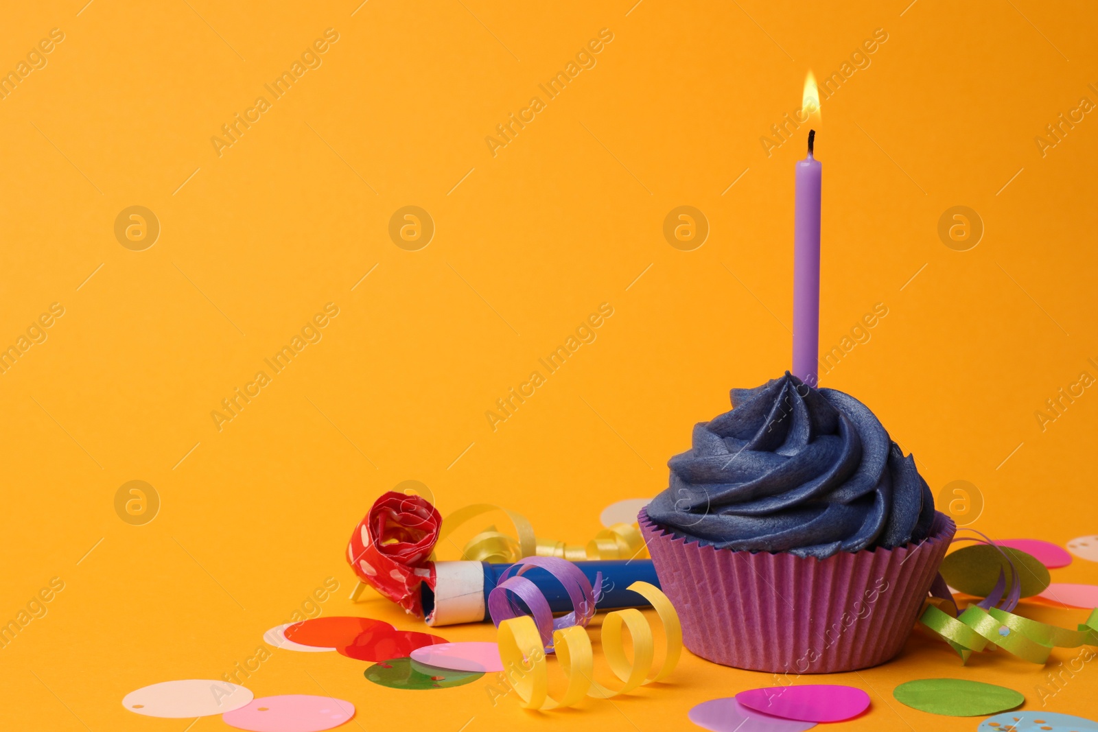 Photo of Delicious birthday cupcake with dark blue cream and burning candle on yellow background. Space for text