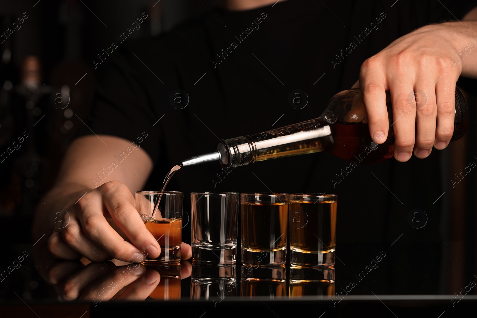 Photo of Bartender pouring alcohol drink into shot glass at mirror bar counter, closeup